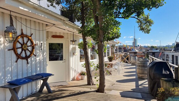 Une terrasse en bois avec un banc, une décoration en forme de roue de navire et un espace barbecue.