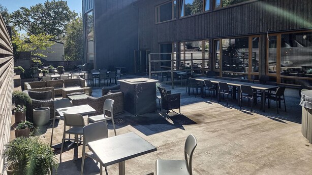 Un patio al aire libre con mesas y sillas, rodeado por un edificio con grandes ventanales.