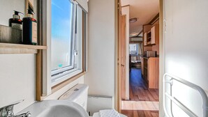 Un baño estrecho con ventana, lavamanos y artículos de aseo en un estante.