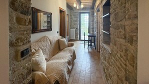 A narrow stone-walled corridor with a sofa, a door, and a table with chairs.