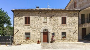 A stone building with a central entrance, two windows with shutters, and a small balcony.