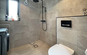 Un baño moderno con ducha, inodoro y dispensador de jabón empotrado.