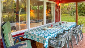 Eine überdachte Terrasse mit Esstisch und Stühlen, umgeben von großen Fenstern mit Blick auf den Garten.