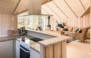 A modern kitchen with a central island, a dining area with a sofa, and a large window providing natural light.