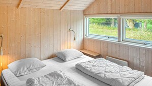 Dormitorio de cabaña de madera con dos camas, un banco y una ventana con vistas a la vegetación.