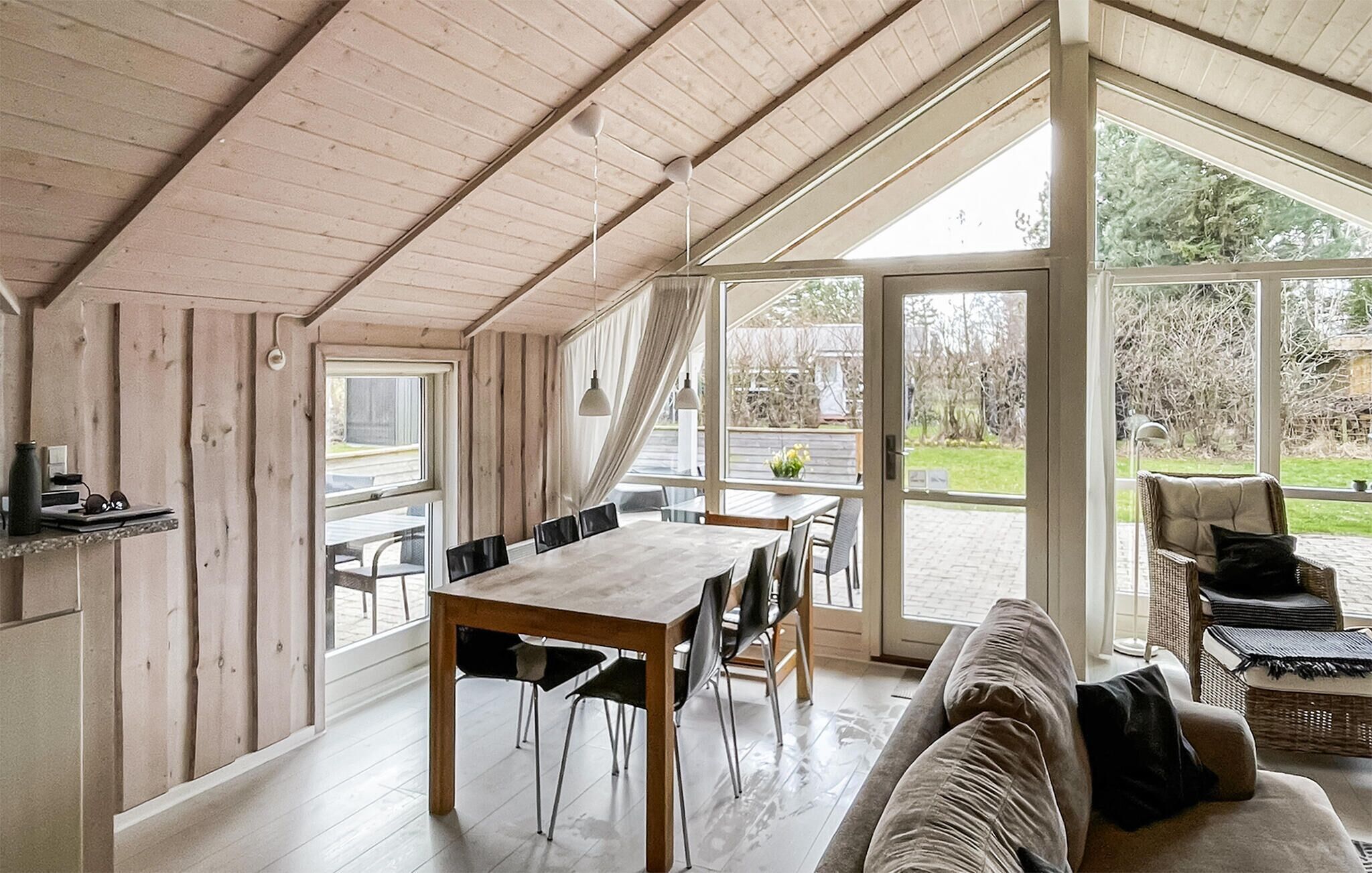 Een ruime kamer met houten plafond, grote ramen, een eettafel en een bank.