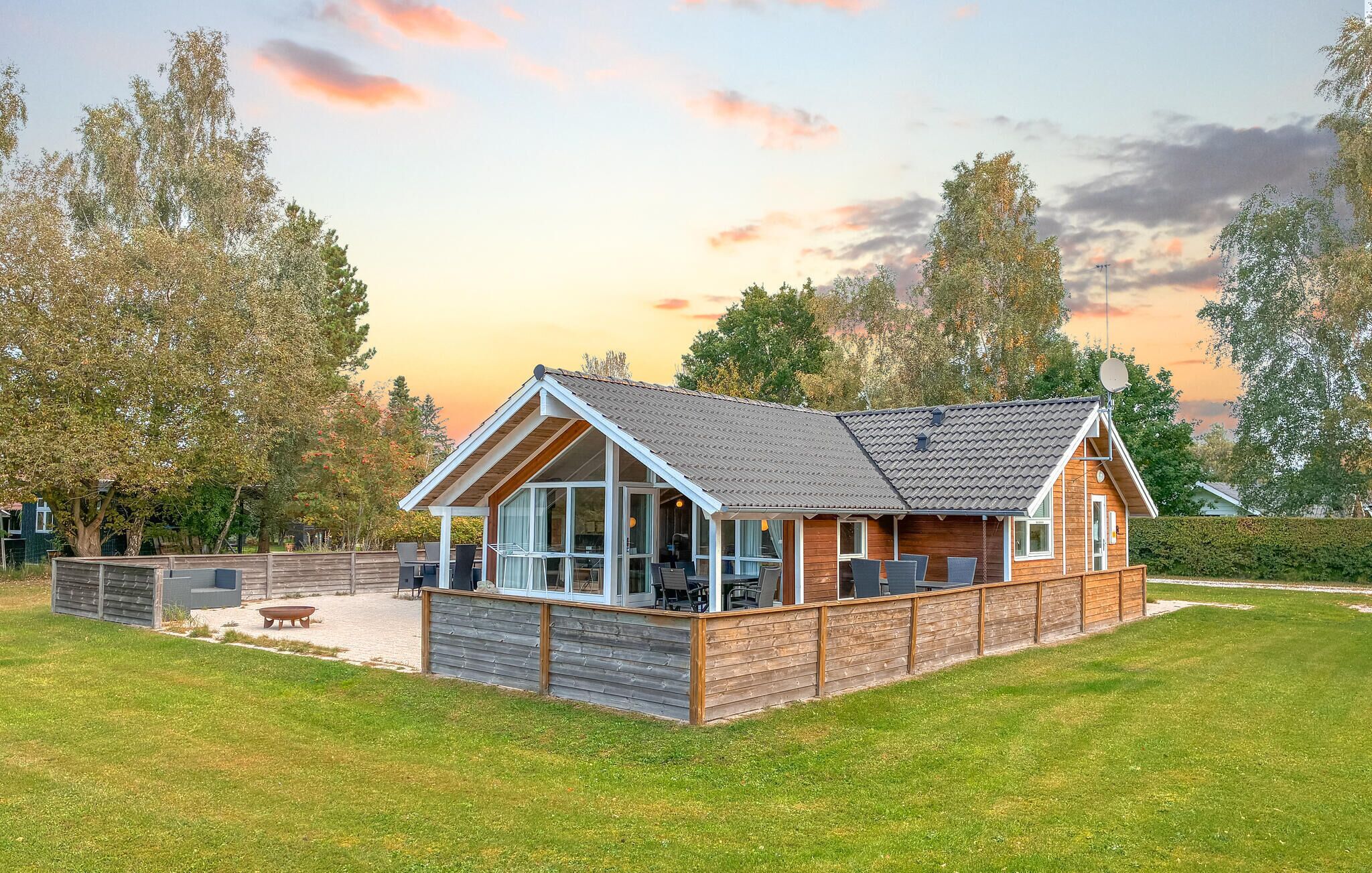 A wooden cabin with a large deck, a covered outdoor seating area, and a view of the surrounding trees.