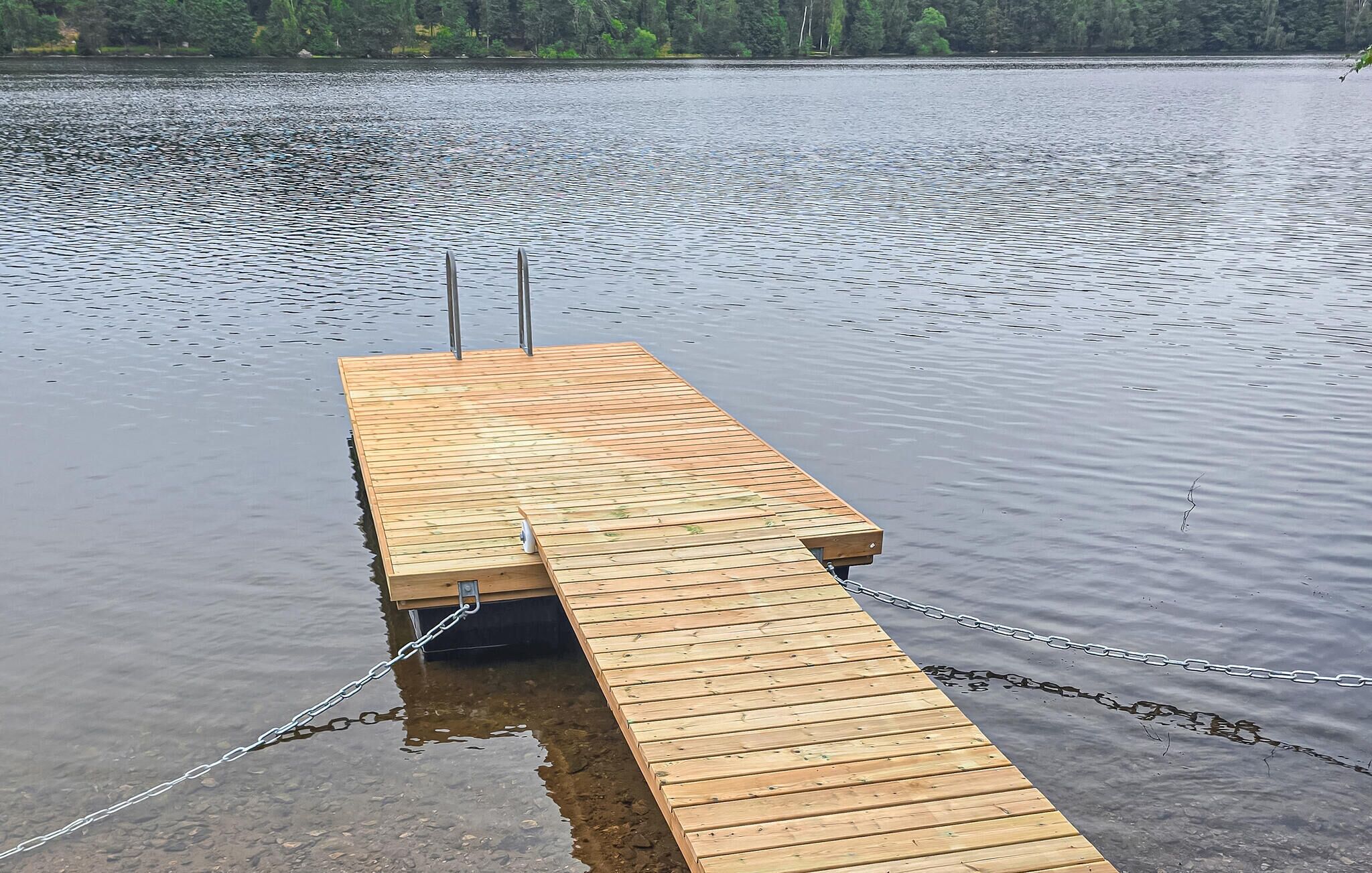 Eine Holzsteg, der sich in ruhiges Wasser erstreckt und mit Ketten gesichert ist.
