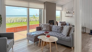 A modern living room with a grey sofa, a round coffee table, and a view of the beach through large windows.