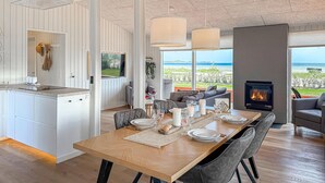 A modern kitchen with a large island, a dining area with a view of the sea, and a fireplace.