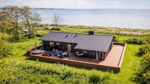 A modern house with a large deck, solar panels, and a view of the sea.