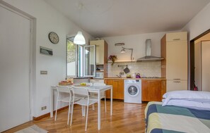 A compact kitchen with a washing machine, a dining area with chairs, and a bed with a quilt.