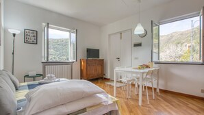 A bedroom with a bed, bedside table, lamp, and a view of a mountainous landscape through a window. - Cozy apartment in Bogliasco with WiFi (Bogliasco)