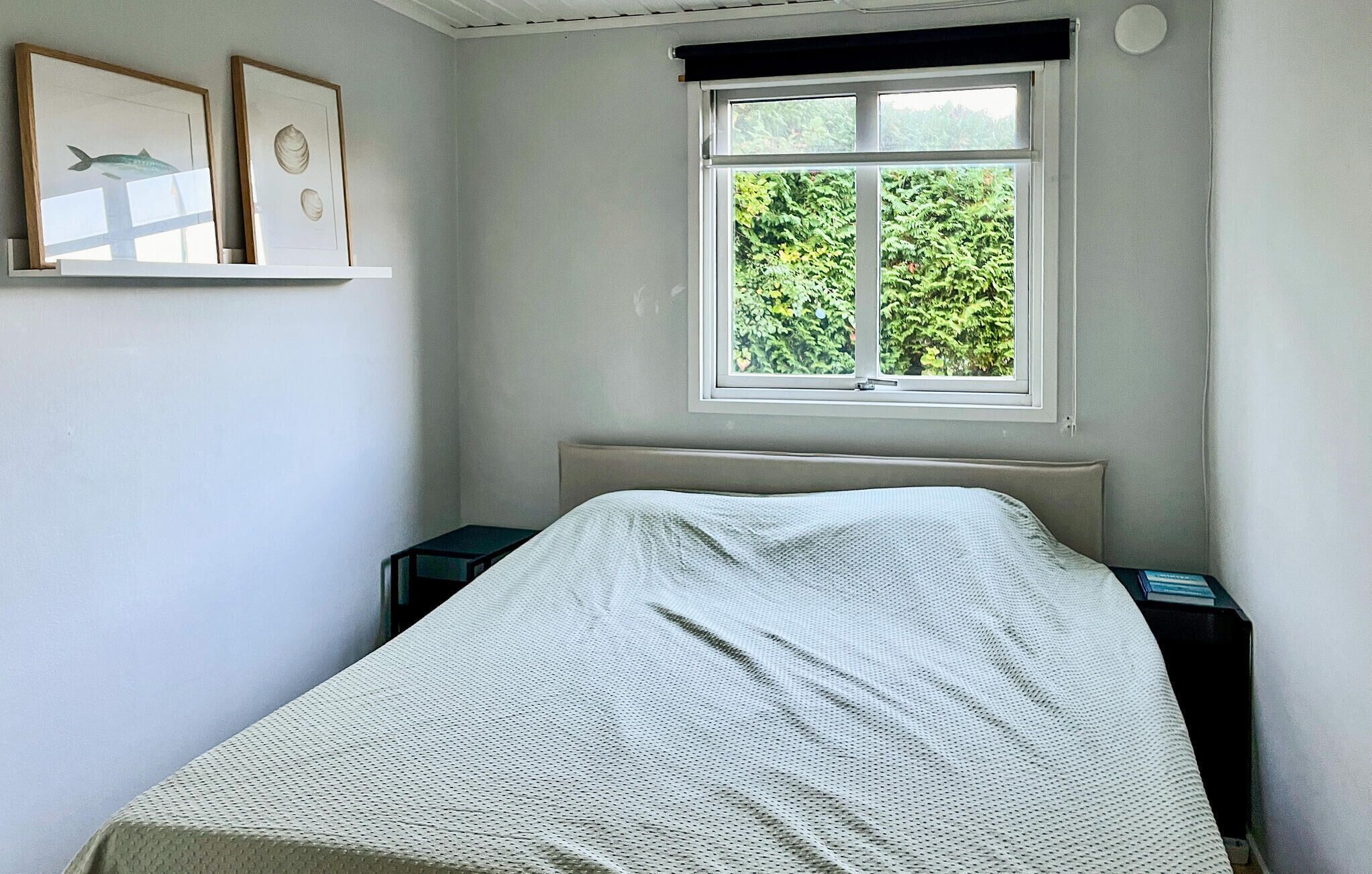 Une chambre à coucher avec un lit, une fenêtre donnant sur un paysage verdoyant et deux tableaux encadrés accrochés au mur.