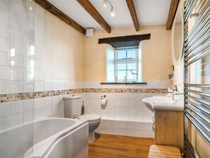 A bathroom with a bathtub, toilet, and sink, wooden beams on the ceiling, and a window with a view.
