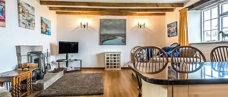 A cozy living room with wooden beams, a fireplace, a TV, and a dining area with chairs and a table.