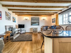 A cozy living room with wooden beams, a fireplace, a TV, and a dining area with chairs and a table.