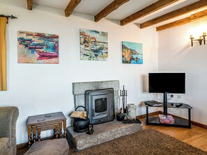 A cozy living room with a fireplace, wooden beams, and three paintings on the wall.