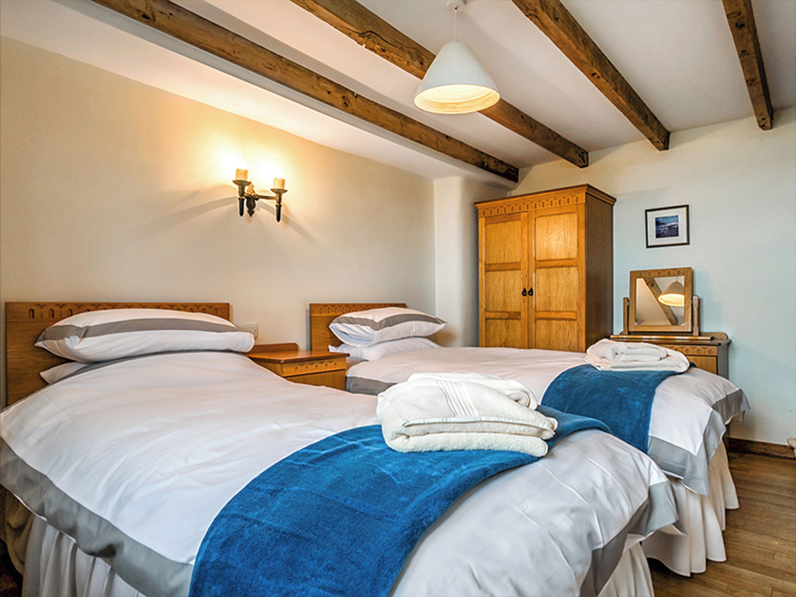 Ein Hotelzimmer mit zwei Betten, Holzbalken an der Decke, einem Kleiderschrank und einer Wandleuchte.