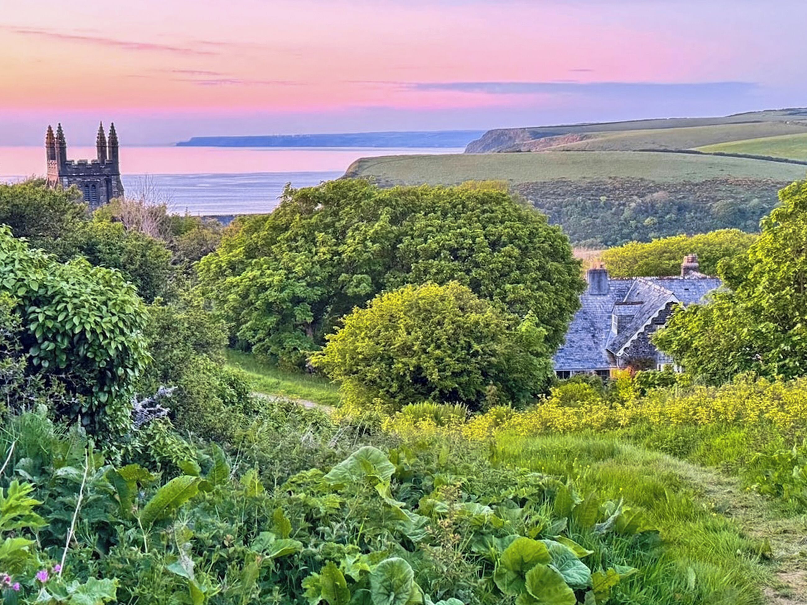 A coastal landscape with a historic tower, lush greenery, and a house with a steep roof.