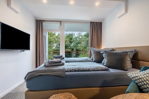 Une chambre moderne avec un grand lit, un téléviseur à écran plat et un balcon agrémenté de rideaux.