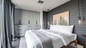 A bedroom with a bed, grey wardrobe, and a cactus painting on the wall.