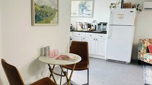 Une cuisine compacte avec un réfrigérateur blanc, une table à manger avec deux chaises et un canapé à motifs floraux.