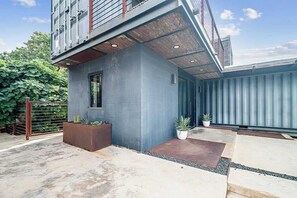 A modern building with a grey facade, a small window, and a concrete patio area with potted plants. - Luxury 4-Bedroom Container Home (Fredericksburg)
