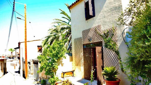 A narrow street with white buildings, a wooden door, and potted plants.