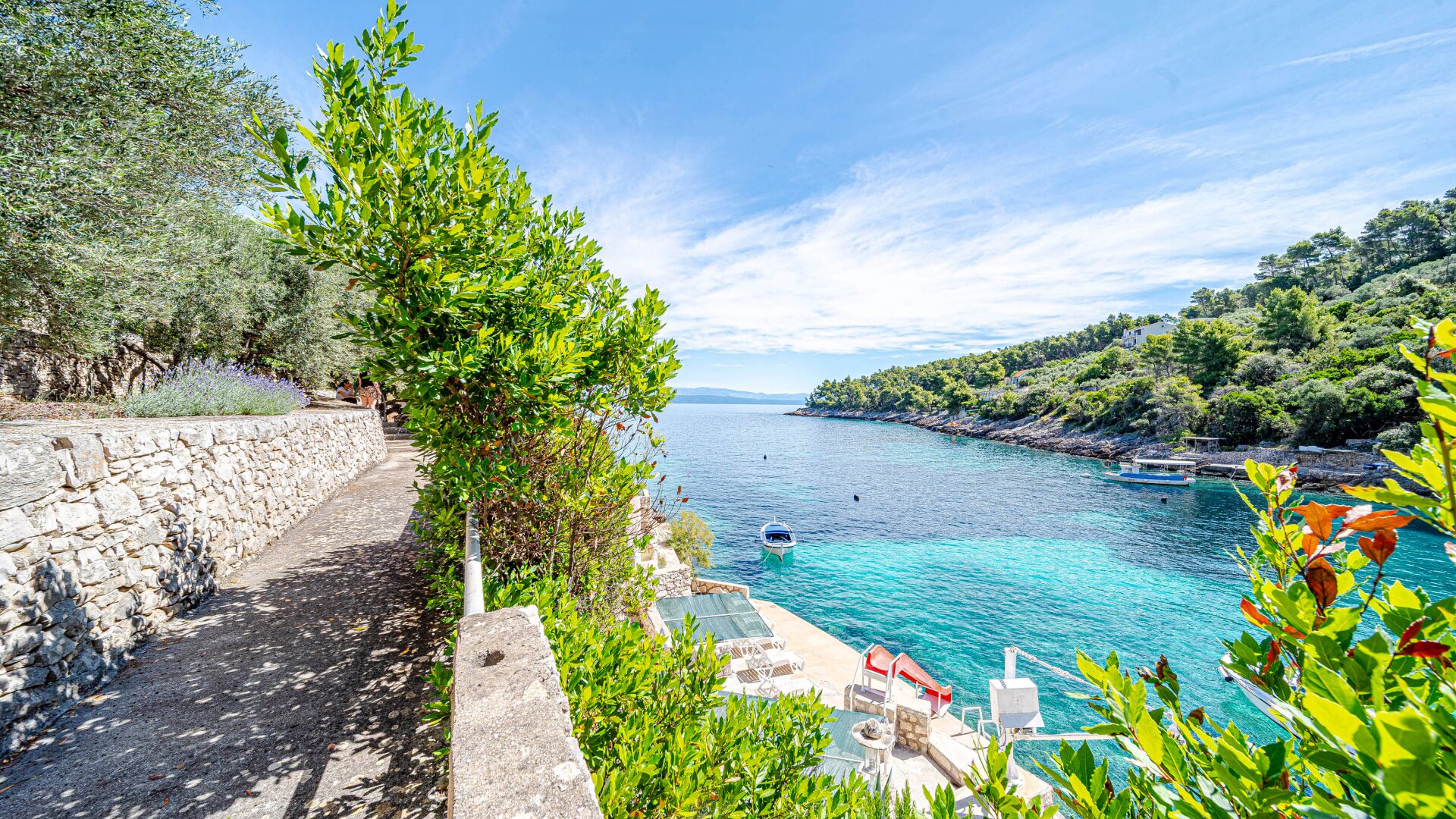 A coastal view with a stone pathway, a boat, and a clear blue sea.