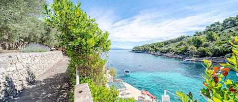 A coastal view with a stone pathway, a boat, and a clear blue sea.