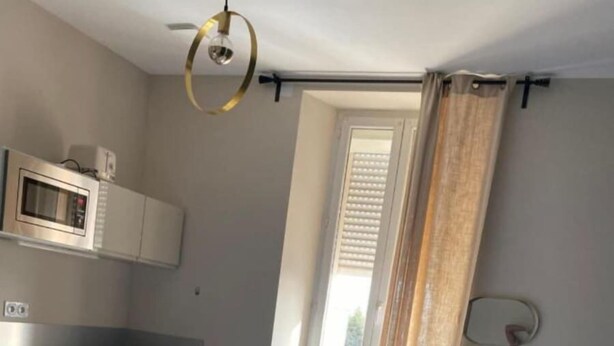 Une chambre d’hôtel comprenant un lit, une kitchenette, une fenêtre avec des rideaux et un luminaire au plafond.