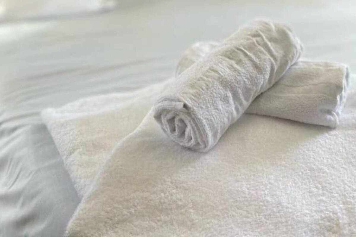 Un lit bien fait, avec du linge de lit blanc et des oreillers, une serviette enroulée posée sur le lit, et un mur de couleur turquoise en arrière-plan.