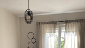 Un salon moderne avec un canapé en cuir noir, une table à manger avec deux chaises, un luminaire suspendu et une fenêtre ornée de rideaux légers.