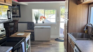 A kitchen with wooden cabinets, a built-in oven, a microwave, and a refrigerator. There is a window with a view of the outside, and a rug on the floor. - Cozy cottage near the falls (Idaho Falls)