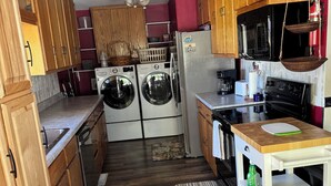 A compact kitchen with wooden cabinets, a washing machine, a refrigerator, a microwave, and a stove. - Cozy cottage near the falls (Idaho Falls)
