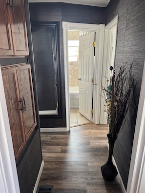 Un couloir doté d’un parquet en bois foncé, de portes blanches et d’un vase contenant des plantes séchées.