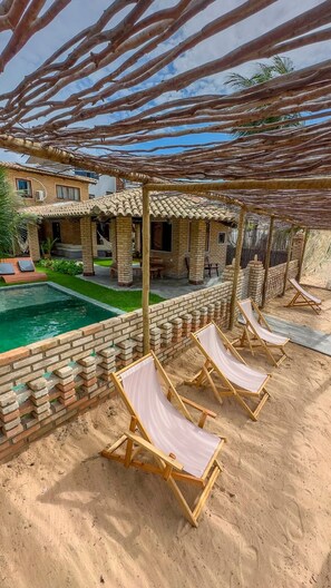 A poolside area with lounge chairs, a brick wall, and a pergola structure. - Beachfront House with Pool and Barbecue in Japaratinga (Japaratinga)