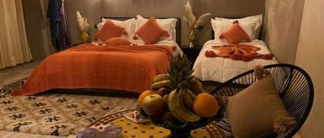 Una habitación de hotel con dos camas, una mesa redonda con fruta y una silla.