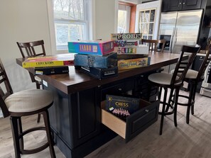 A kitchen with a wooden island, chairs, and a variety of board games.