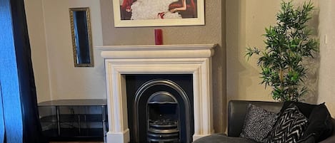 Una sala de estar con chimenea, un sofá, una mesa y un cuadro en la pared.
