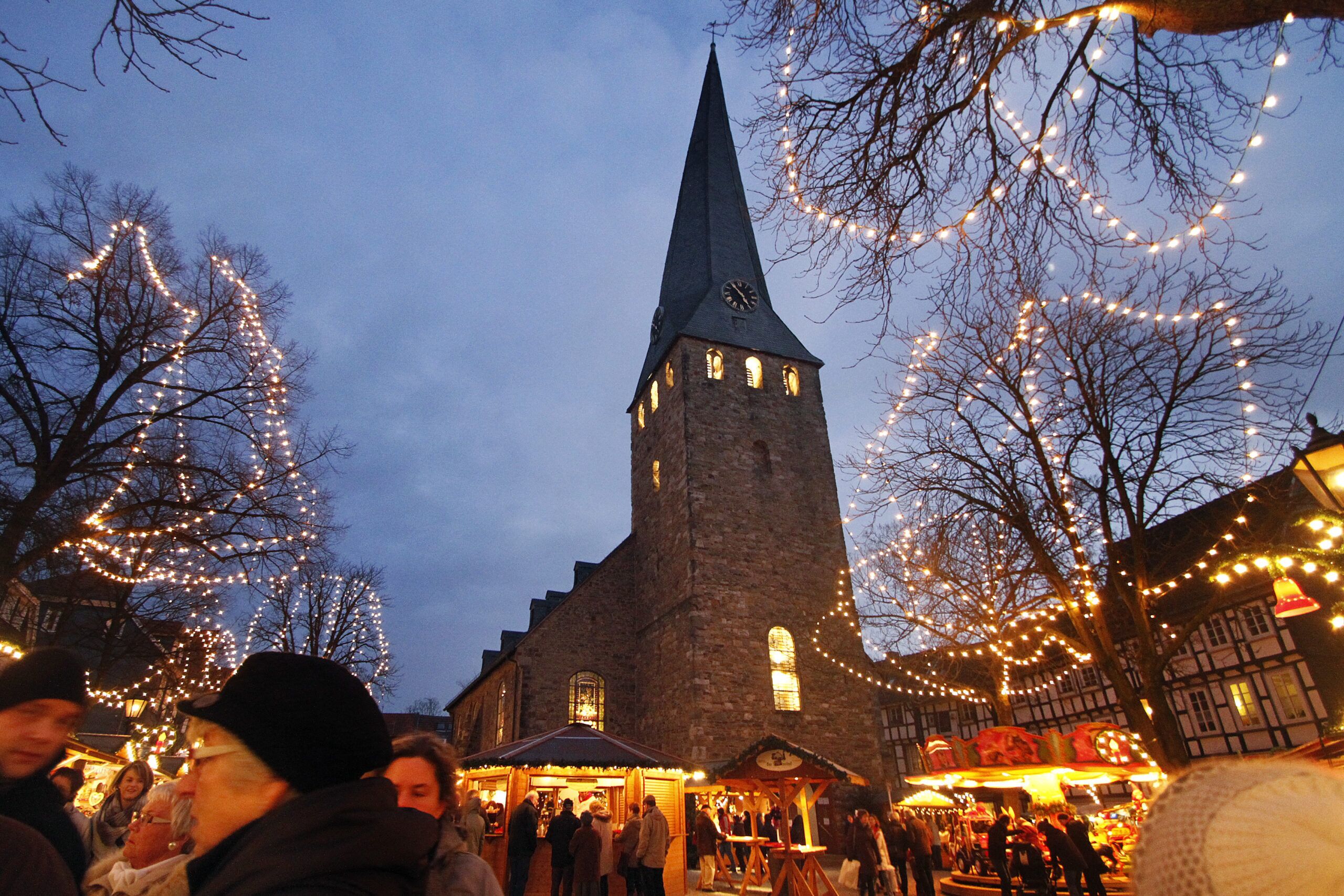 Un bâtiment historique doté d’une tour horlogée, entouré d’arbres décorés de guirlandes lumineuses, ce qui témoigne d’une ambiance festive.
