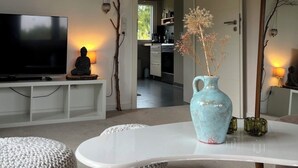 A modern living room with a flat-screen TV, a Buddha statue, a vase with dried flowers, and a large mirror. - Natural paradise at the gateway to the Ruhr area: Idyllic temporary home on the Heierberg (Hattingen)