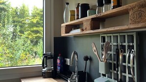A modern kitchen with a large window, a built-in sink, and wooden shelves holding kitchen items. - Natural paradise at the gateway to the Ruhr area: Idyllic temporary home on the Heierberg (Hattingen)