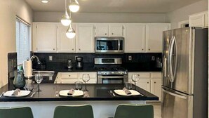 A modern kitchen with white cabinets, a central island with bar stools, stainless steel appliances, and pendant lighting. - 3BR/3BA w/ Pool & BBQ • 15 Mins to Strip & Airport (Las Vegas)