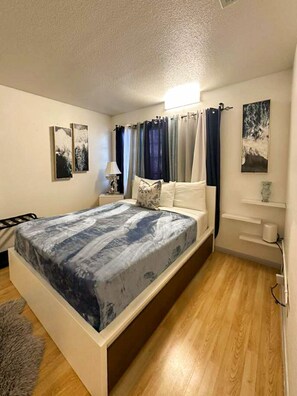Um quarto com uma cama, uma mesa de cabeceira, uma luminária, uma prateleira com um vaso e um quadro na parede.