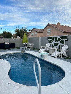 Uma piscina com ofurô integrado, rodeada por espreguiçadeiras brancas e um guarda-sol verde.
