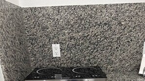 Une cuisine dotée de plans de travail en granit, d’une cuisinière électrique à deux plaques et de meubles blancs.