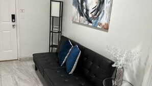 Un salon moderne avec un canapé noir, un vase en verre contenant des fleurs blanches et un tableau abstrait accroché au mur.