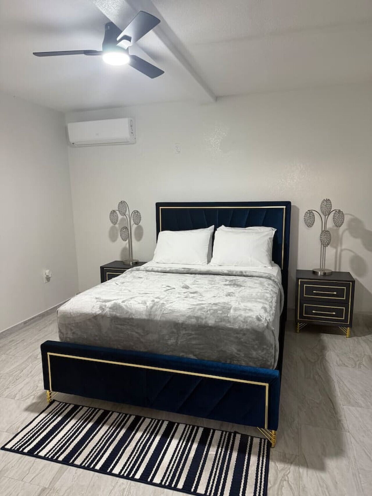 A bedroom with a bed, a ceiling fan, a nightstand, and a decorative metal piece on the wall.